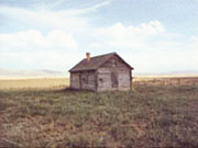 A Log cabin sits in the middle of a flat lonely field